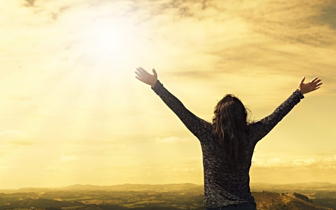 A woman raising her hands in the air looking into the sun