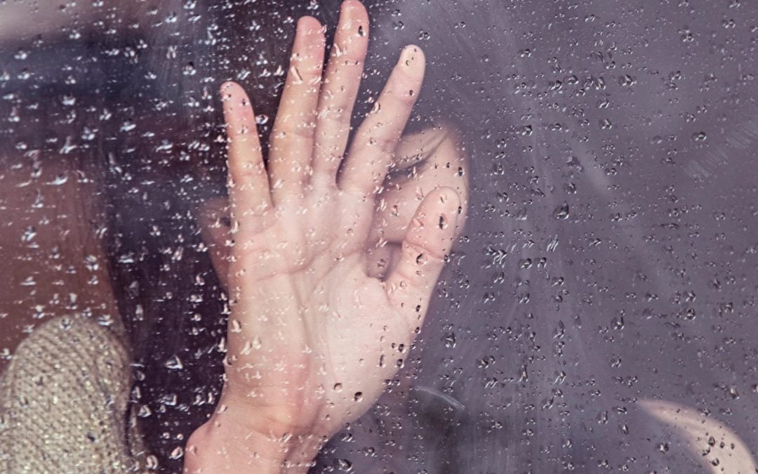 A woman with her head down and hand against a water-covered window