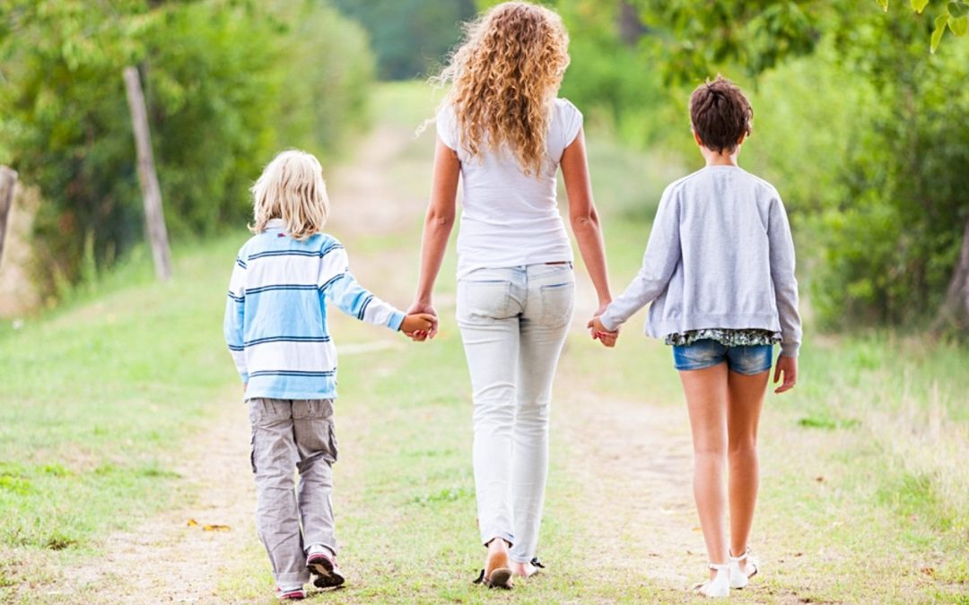 Mom walking on path holding hands with and flanked by two kids