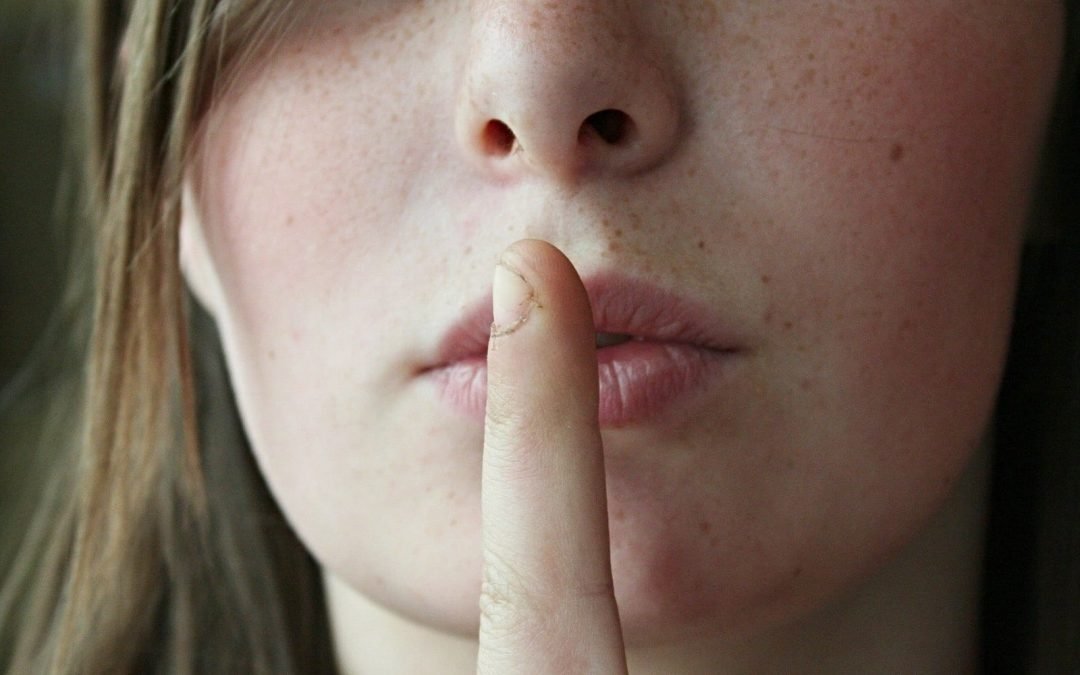White woman with fingers to her lips in silence