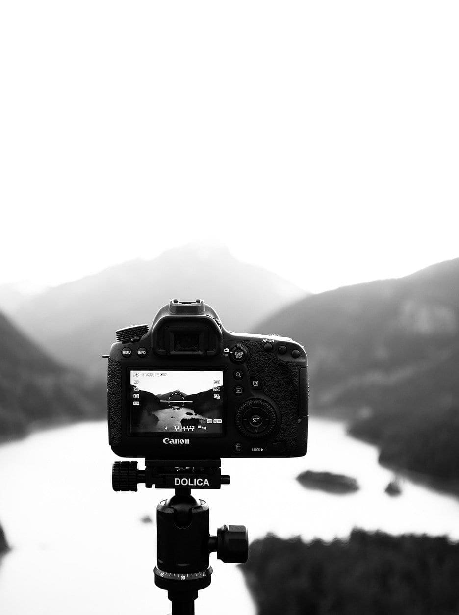 A camera taking a photo of a lake with mountains in the background