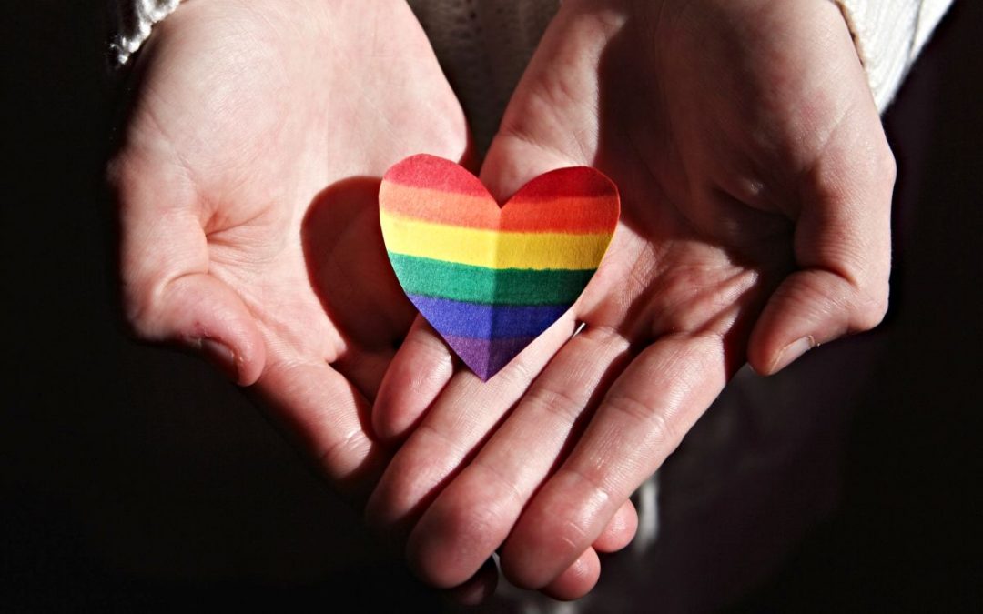 Two hands holding a paper rainbow heart