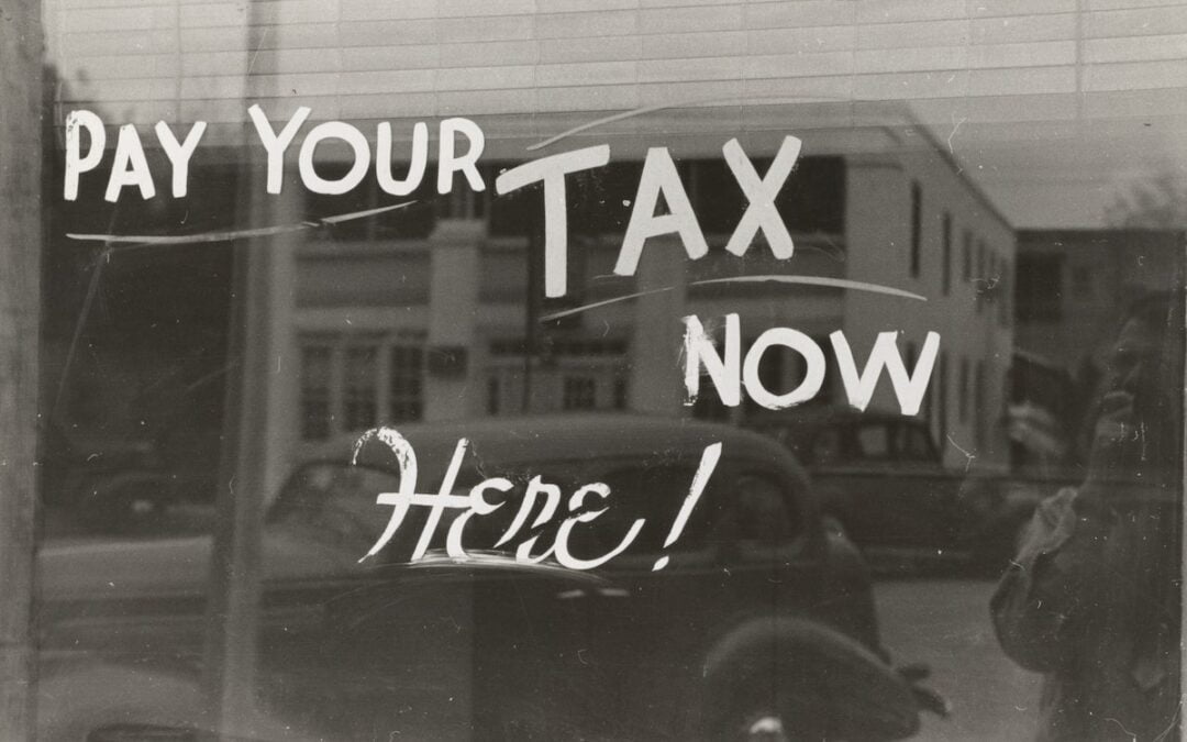 A shop window with the words “Pay your tax now here!” displayed in white lettering.