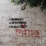 A concrete wall with the phrase, “If you repeat a lie often enough it becomes politics” on it.
