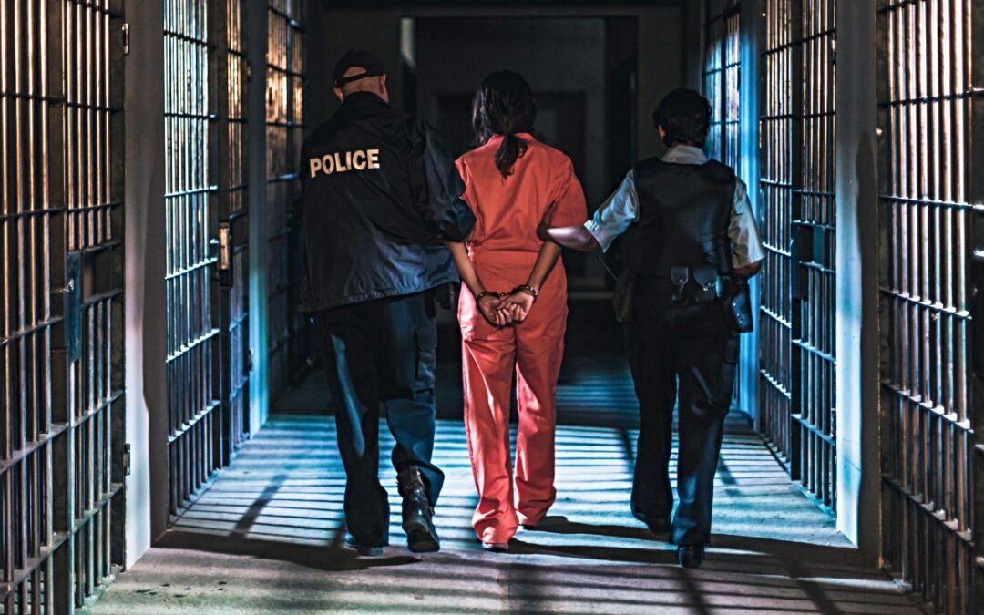 Prisoner in orange jumpsuit escorted by two police officers