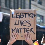 A man holding a cardboard sign that says, “LGBTIQ+ Lives Matter.”