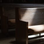 A row of church pews in a dark room with a single sunspot shining down.