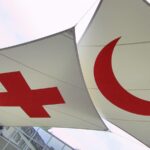 A red cross and red crescent symbol on two white pieces of fabric suspended in the air.