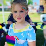 A picture of a little girl with a rainbow painted on her cheek.