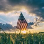 A U.S. flag sitting in a field with the sun rising in the background.