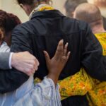 A group of people, seen from behind, in a group hug during a memorial service.