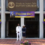 A press photo from the “mockumentary” film “Honk for Jesus. Save Your Soul.” Two people are standing outside a church with a “Welcome Back” sign over the entrance.