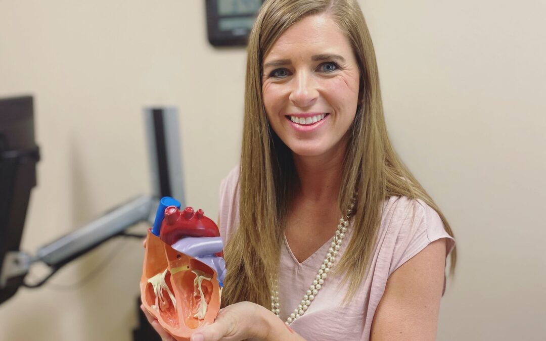A woman sitting in a doctor’s office holding a model of a heart.