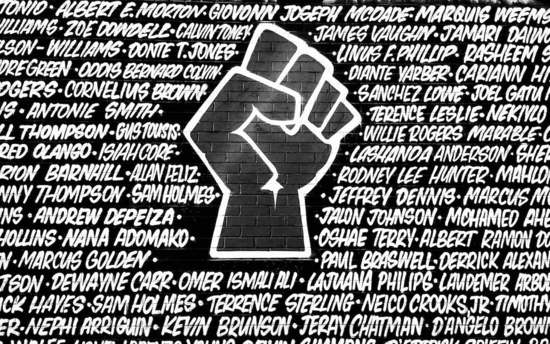 The outline of a fist in white paint on a wall surrounded by names.