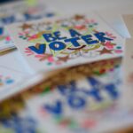 A stack of white cards with “Be a Voter” on them and a colorful illustration around the words.