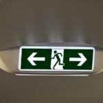 A black-and-white exit sign showing the figure of a person moving in the direction of the arrow.