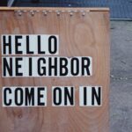 A wooden sign with block lettering that says, “Hello neighbor. Come on in.”