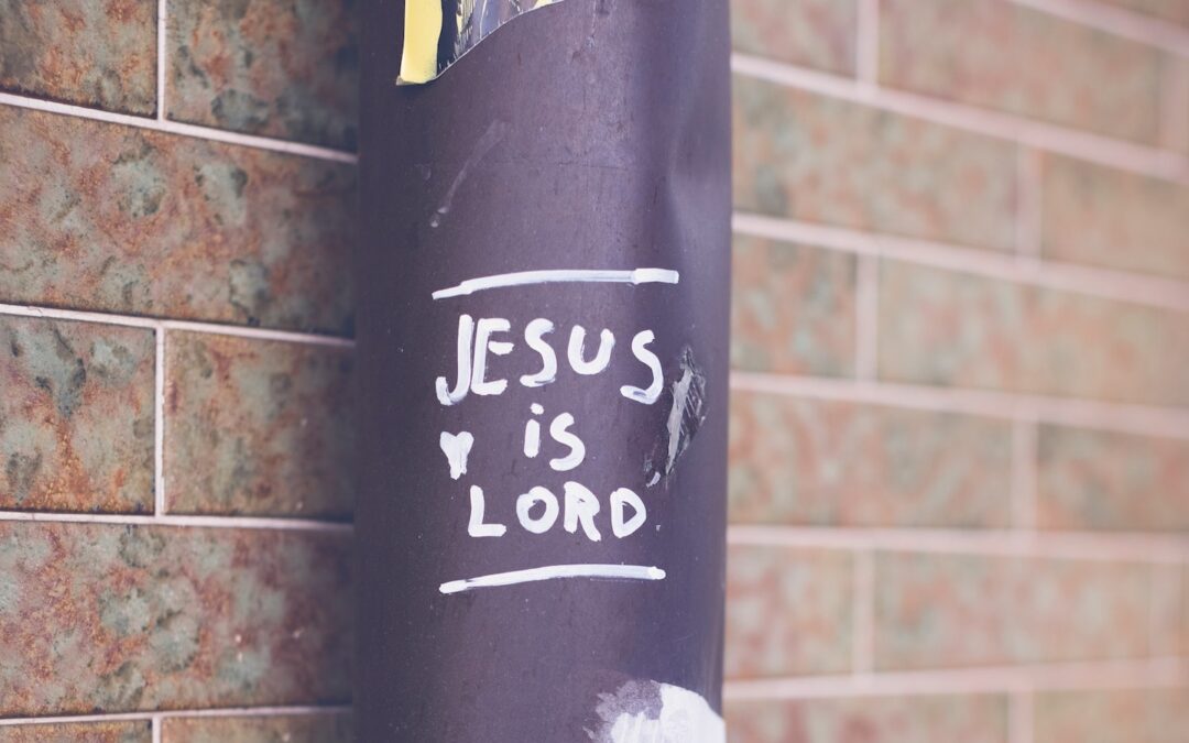 The statement, “Jesus is Lord,” written on a black pole standing next to a red brick wall.