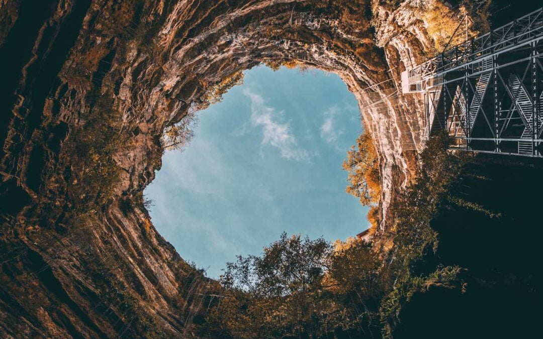 The sky seen from the bottom of a cave with rock cliffs on all sides.