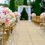 A venue set up for a wedding with chairs arranged to create a center aisle, flowers and an arbor with white linen draped over it.