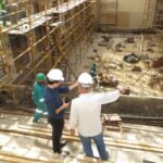 Two men standing at a construction site looking over the progress and pointing at something at the site.