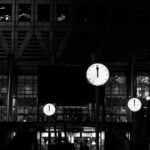 A black-and-white image of multiple clocks at midnight outside an office building.
