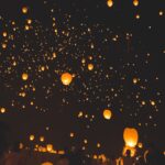 Paper lanterns illuminated by candles being released into the night sky.