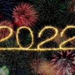 The year 2022 in yellow fireworks with lots of multi-colored fireworks in the background.