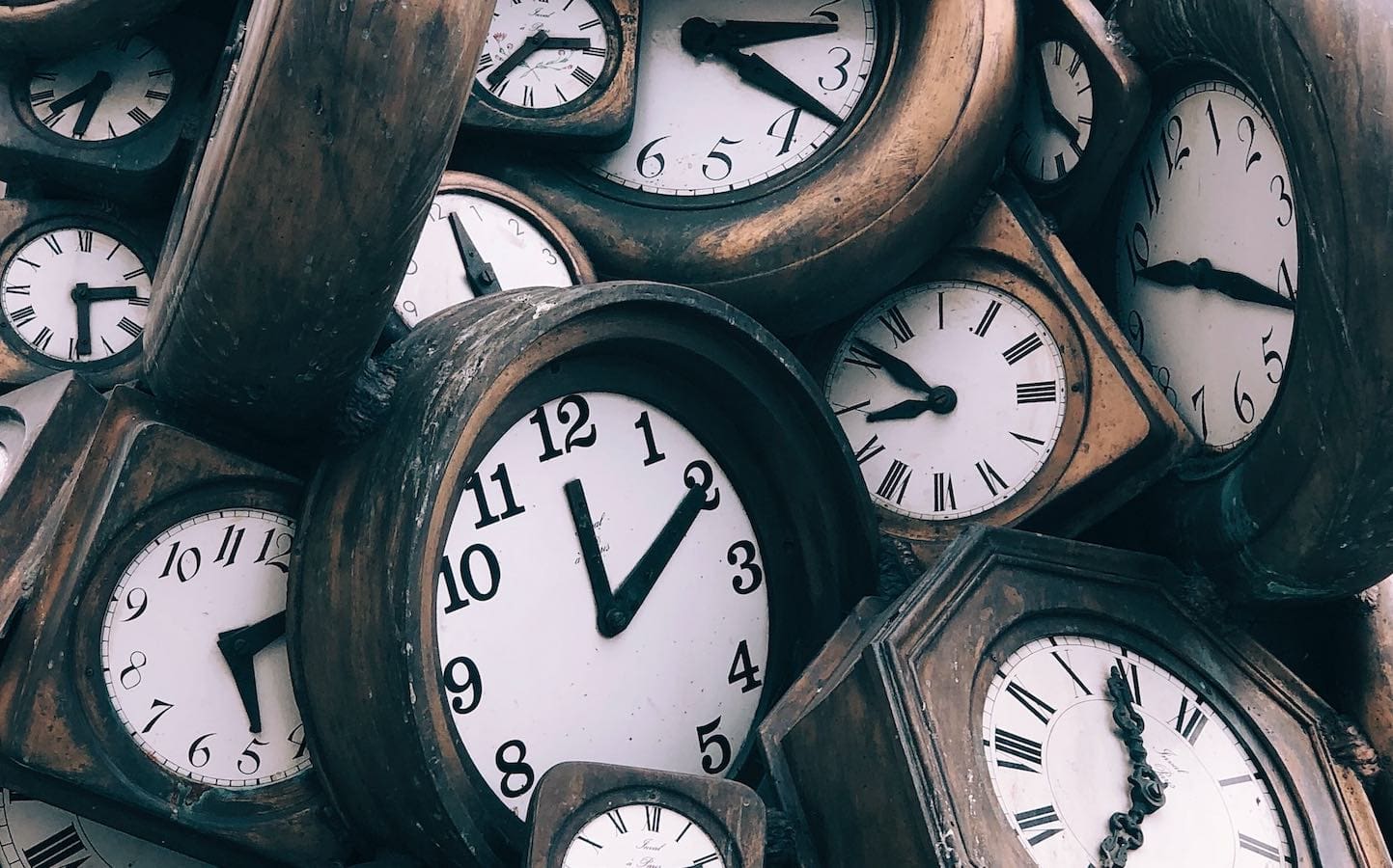 Many analog clocks sitting in a pile showing various times.