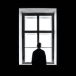 Black and white image of man looking out of a window.