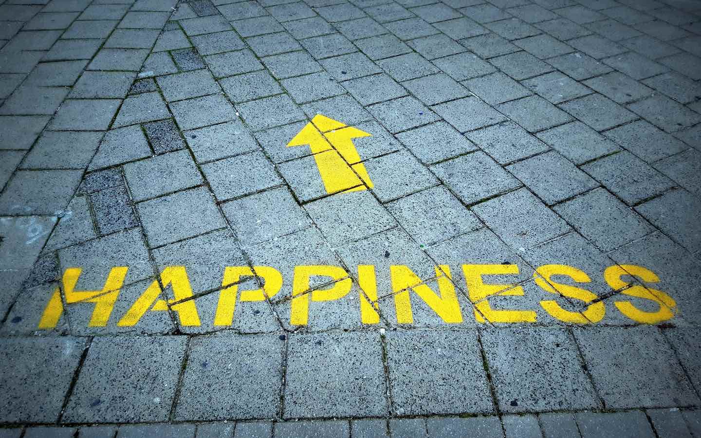 The word “happiness” painted in yellow on pavement.