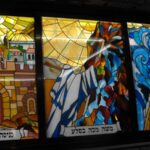 A series of three stained glass windows depicting (right to left): Crossing of the Red Sea, Moses striking the rock, and Jerusalem.