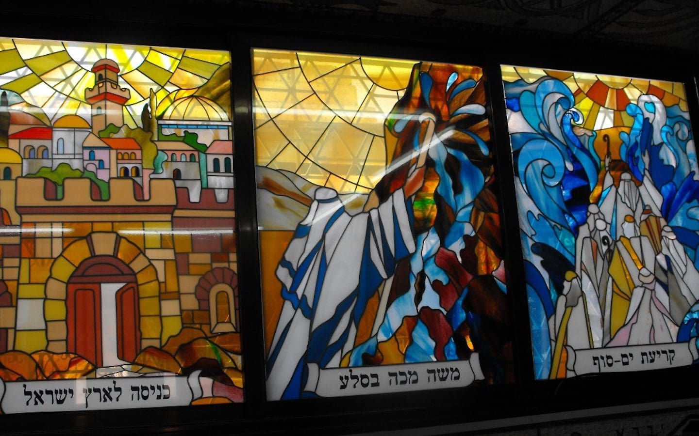 A series of three stained glass windows depicting (right to left): Crossing of the Red Sea, Moses striking the rock, and Jerusalem.