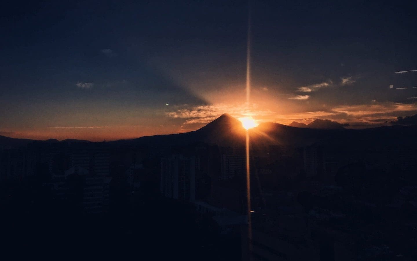 The sun rising over mountains with darkness in the foreground and light in the background.