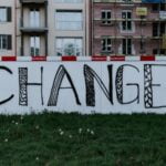 A white concrete wall on which the word “change” is spray painted.