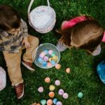 Two children sitting on the ground with easter eggs and baskets next to them seen from above.