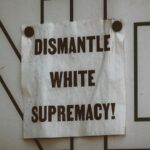 A white sign on a wall with bold, capital lettering that says, “Dismantle white supremacy!”
