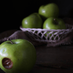 One rotten apple alongside a basket of apples.