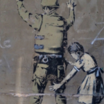 A mural on the west bank wall of a girl frisking a police officer.