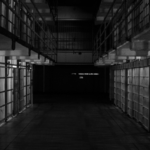 A black and white photo of an empty corridor of prison cells