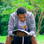 A man sitting on a park bench reading the Bible.