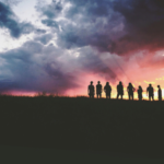 A photo of several people on a hill at sunset standing together.