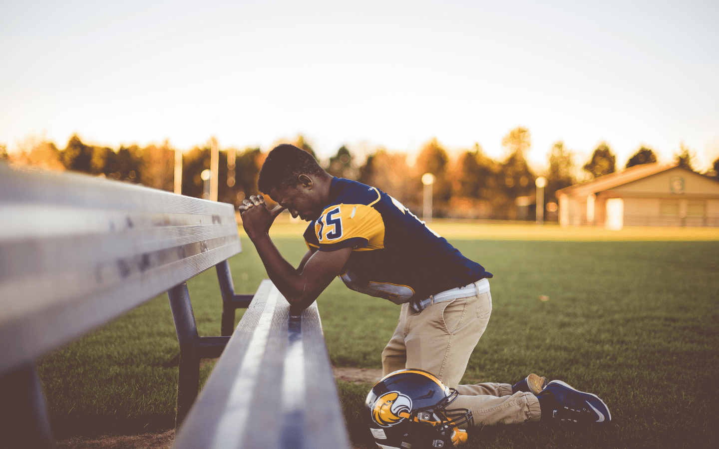 A young football player praying on a sideline bench.