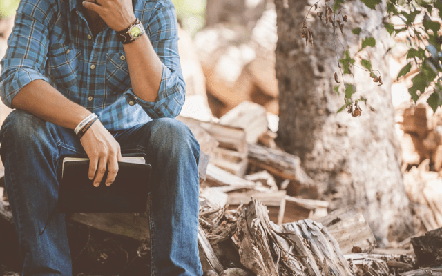 Man sitting down in the woods with a book in his hand
