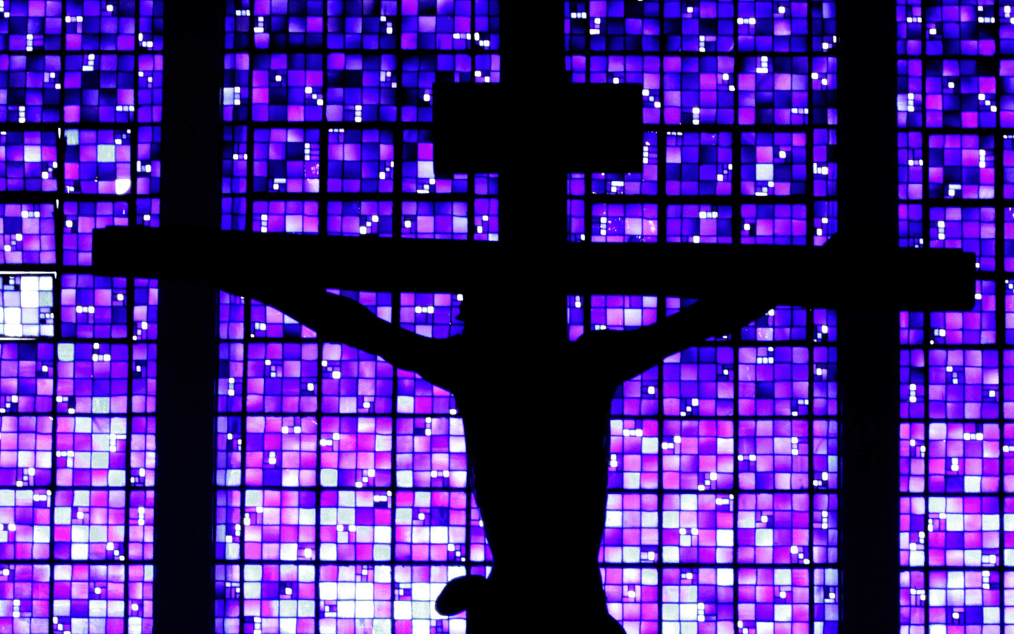 A silhouette of a cross with a blue-tinted stained glass window in the background.