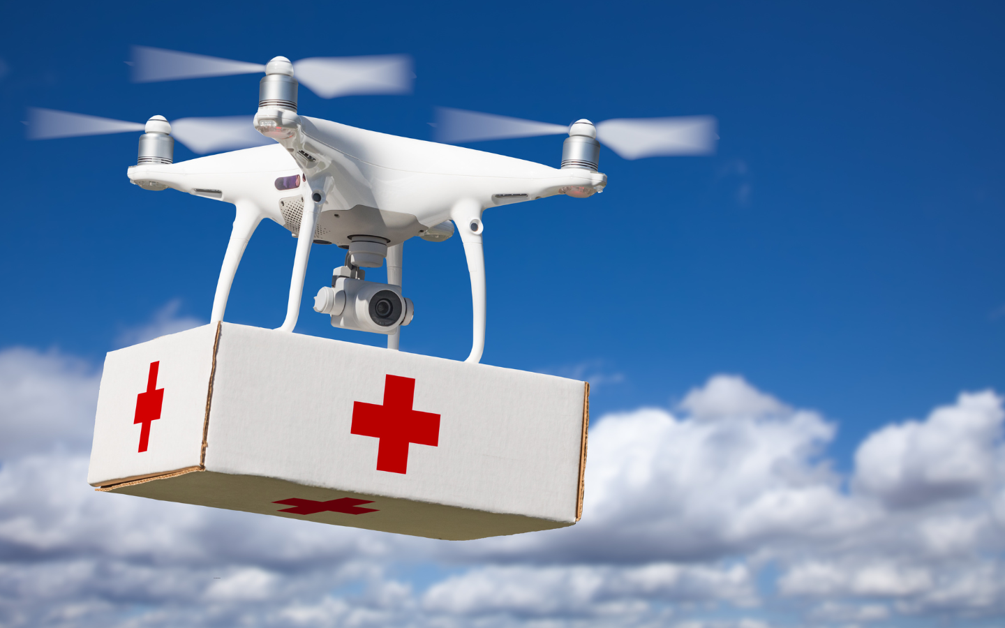 A drone carrying a Red Cross box of supplies.