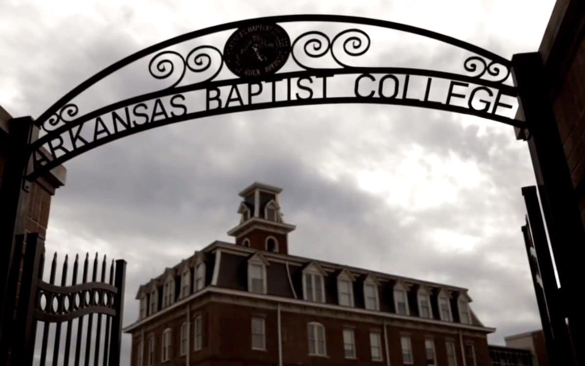 The exterior of a building in the background with a metal arch in the foreground over the sidewalk entrance with the words “Arkansas Baptist College.”