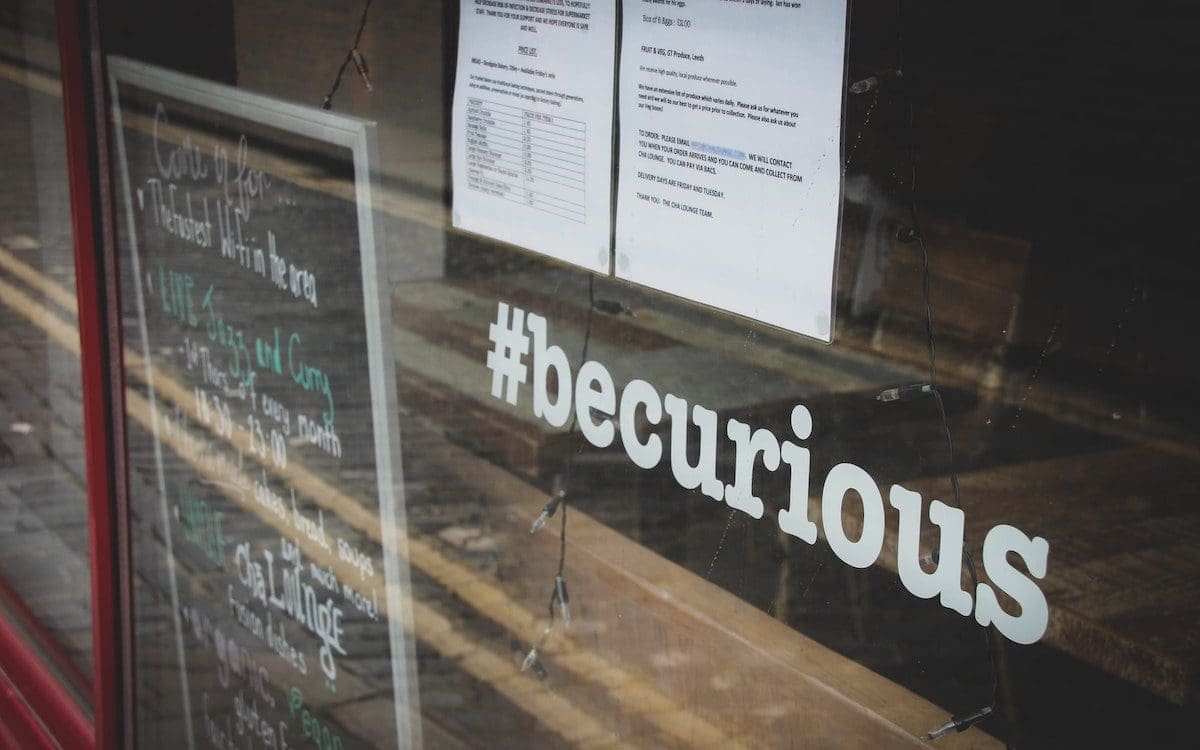 The hashtag #becurious on the window of a store.
