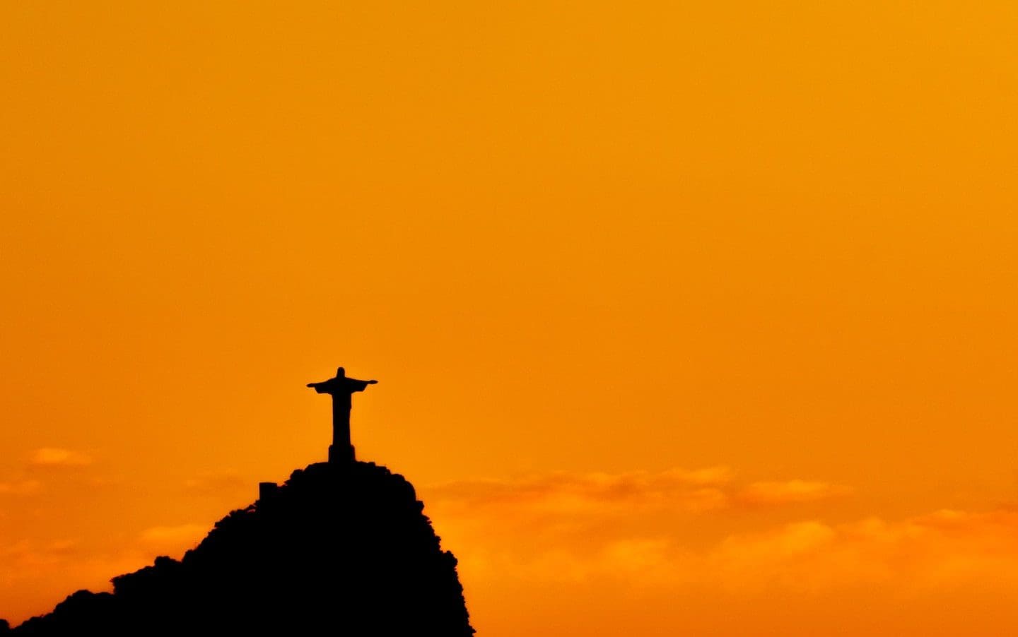 The Christ the Redeemer statue in silhouette at sunset.