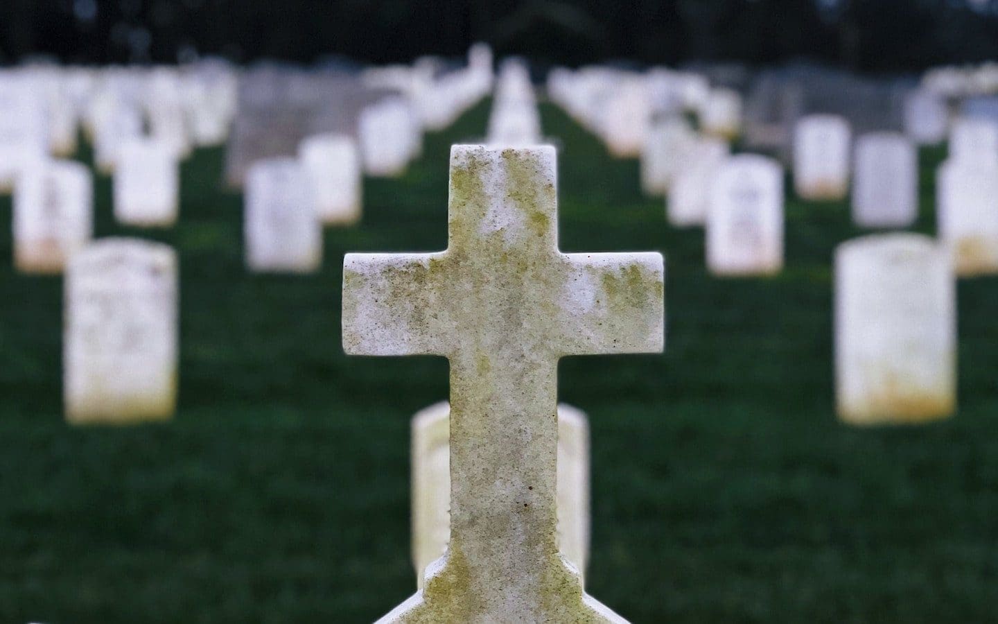 A cross on the top of a gravestone in a cemetery with other gravestones in the background.
